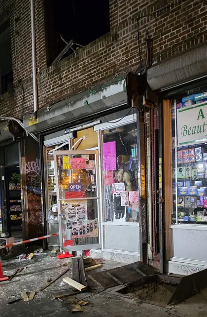 The damaged storefront after the fire: the door frame blown out, debris across the sidewalk, and the shop sign still in place.